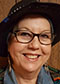 Charlene Willing McManis headshot. Charlene, a light-skinned indigenous woman, wears a hat, glasses, and dangly earrings.