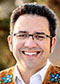 Richard Van Camp headshot. Richard is a light-skinned native man with short brown hair, glasses, a white button-up shirt under a colorful vest.