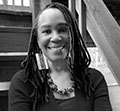 Tracy Occomy Crowder black and white author photo shows tracy sitting on steps outside with hair in braids wearing a chunky necklace and earrings and a long-sleeve shirt.