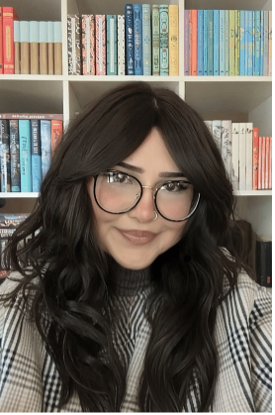 Headshot of Layla Fallah-Cyphert with long brown hair and glasses in front of colorful bookshelves